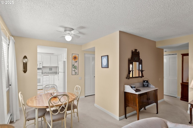 dining room featuring a ceiling fan, light colored carpet, a textured ceiling, and baseboards