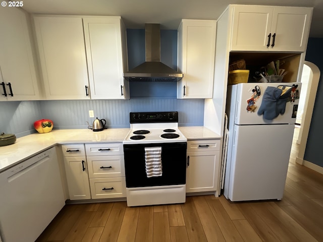 kitchen with light wood-type flooring, white appliances, white cabinetry, and wall chimney range hood