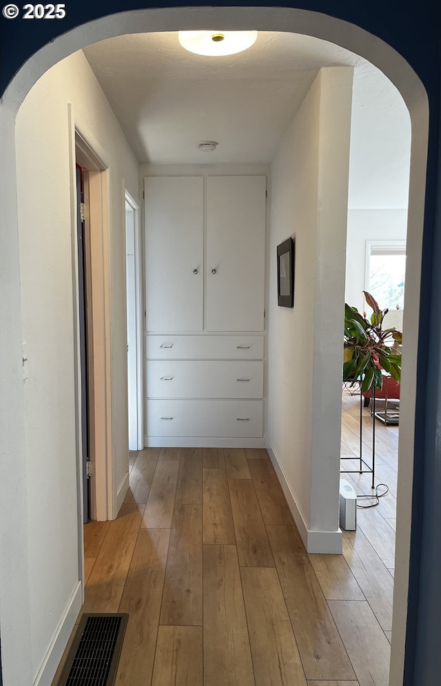 hallway featuring arched walkways, light wood-style floors, visible vents, and baseboards