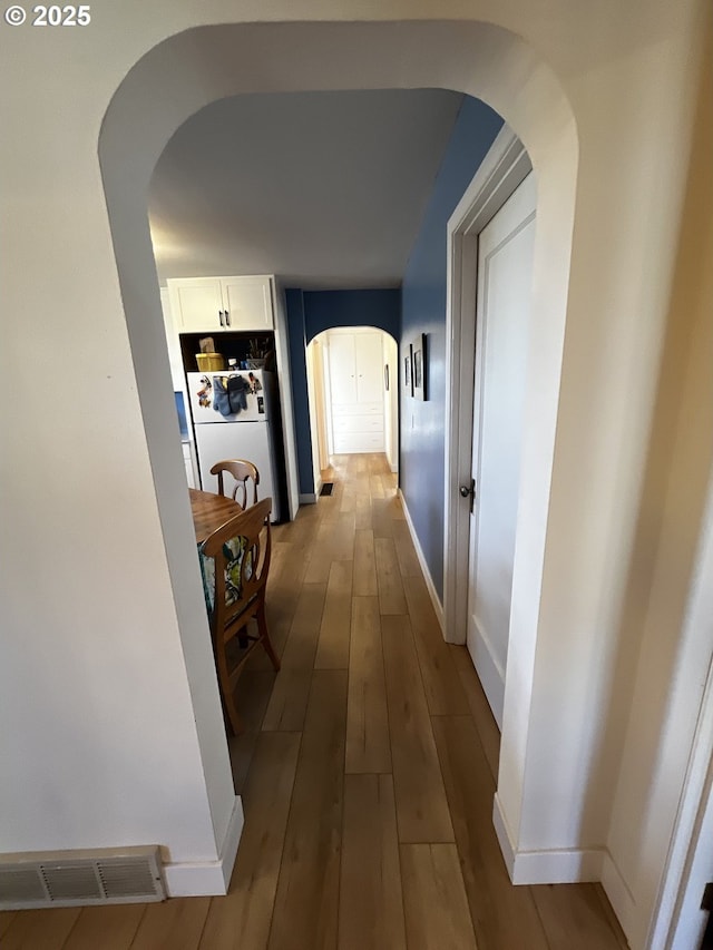 corridor featuring light wood-type flooring, arched walkways, visible vents, and baseboards