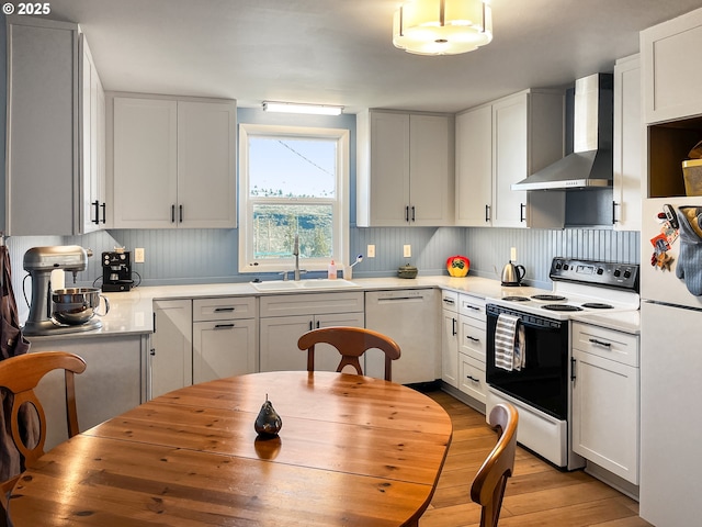 kitchen with wall chimney range hood, a sink, white appliances, light wood-type flooring, and white cabinets