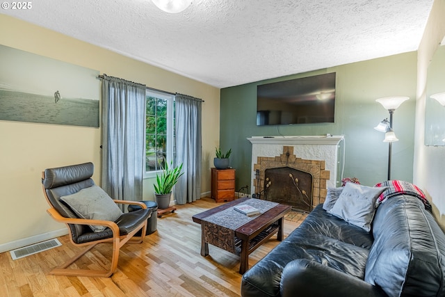 living room with visible vents, a textured ceiling, wood finished floors, a fireplace, and baseboards