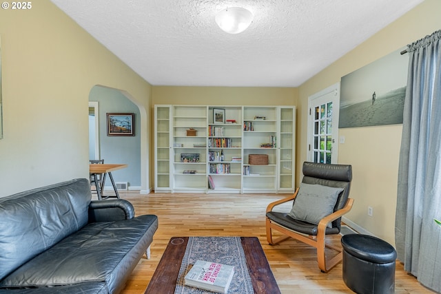 living room featuring baseboards, wood finished floors, arched walkways, and a textured ceiling