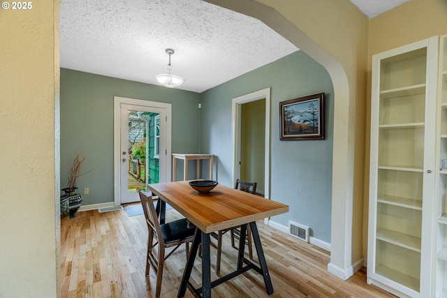 dining area with visible vents, baseboards, wood finished floors, arched walkways, and a textured ceiling