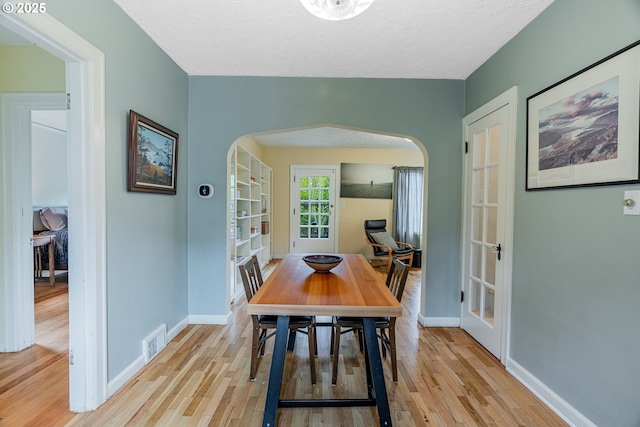 dining space featuring baseboards, visible vents, arched walkways, and light wood-type flooring