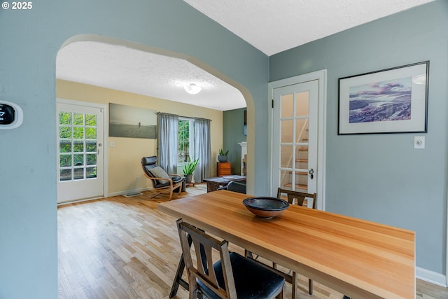 dining room with arched walkways, a textured ceiling, baseboards, and wood finished floors