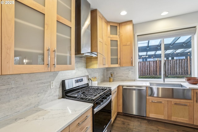 kitchen featuring light stone countertops, appliances with stainless steel finishes, wall chimney exhaust hood, decorative backsplash, and sink