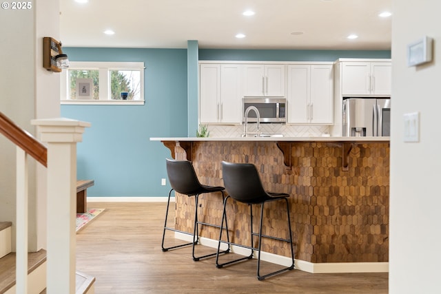 kitchen featuring a breakfast bar, white cabinets, light wood-style floors, appliances with stainless steel finishes, and tasteful backsplash