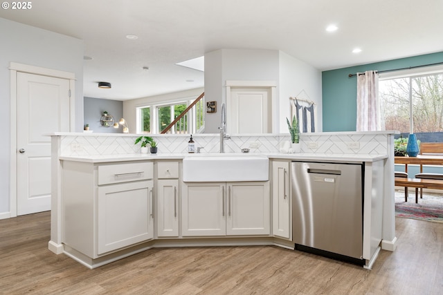 kitchen with light wood finished floors, decorative backsplash, dishwasher, light countertops, and a sink