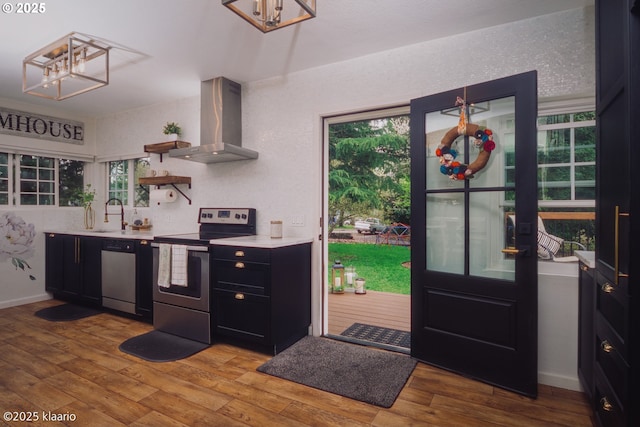 kitchen with wall chimney range hood, stainless steel appliances, light wood-type flooring, and a chandelier