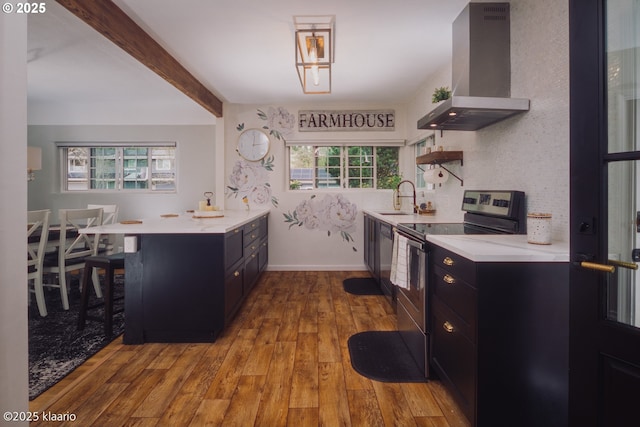 kitchen featuring electric range, light countertops, wall chimney exhaust hood, dark cabinetry, and a sink