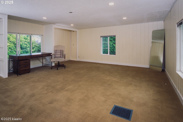 living area featuring carpet flooring, a textured ceiling, visible vents, and plenty of natural light