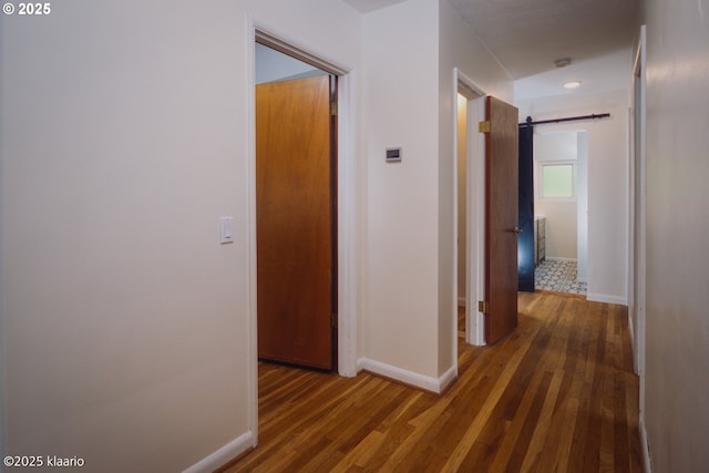 hallway featuring baseboards, a barn door, and wood finished floors