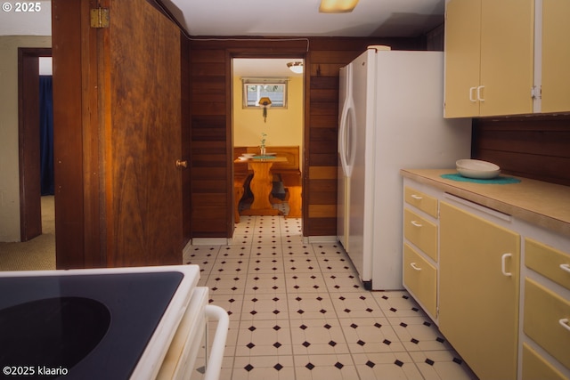 kitchen with light countertops, wood walls, freestanding refrigerator, and light floors