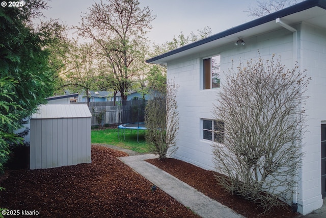 view of property exterior with concrete block siding, a trampoline, an outdoor structure, and a shed