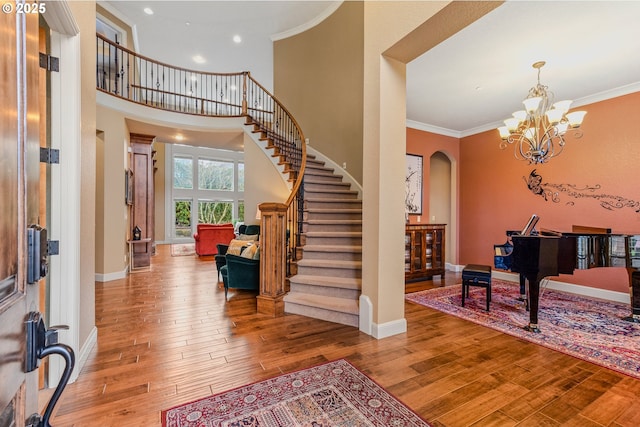 entryway with arched walkways, baseboards, stairs, wood-type flooring, and crown molding