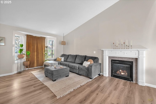 living room featuring vaulted ceiling, a tile fireplace, wood finished floors, and baseboards