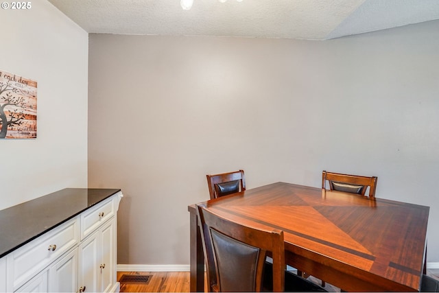 dining space featuring light wood-style floors, baseboards, and a textured ceiling