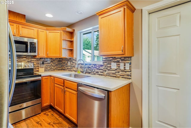kitchen featuring appliances with stainless steel finishes, a sink, decorative backsplash, light wood finished floors, and recessed lighting