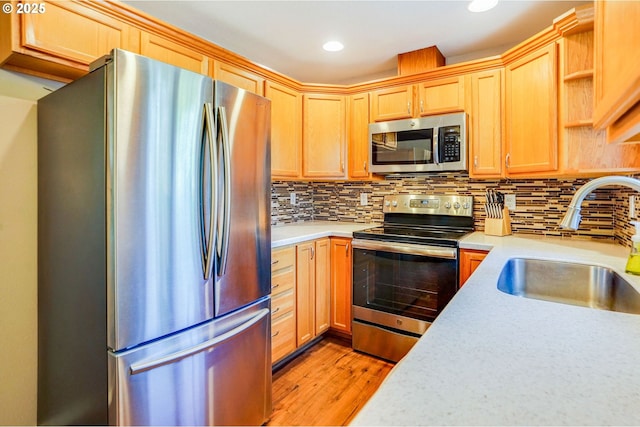 kitchen with appliances with stainless steel finishes, a sink, light countertops, light wood-style floors, and recessed lighting
