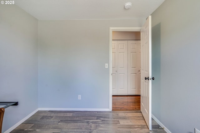 empty room with wood finished floors, a smoke detector, and baseboards