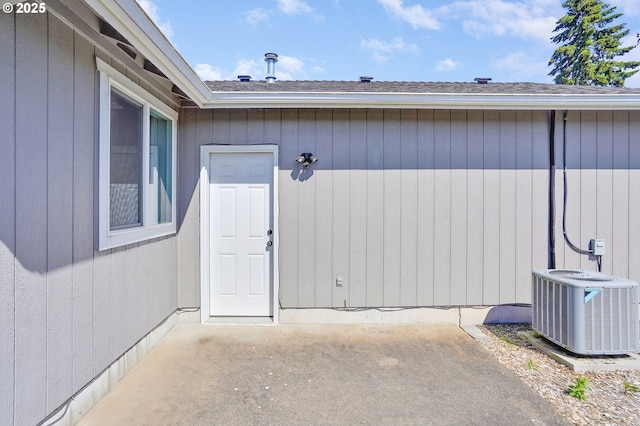 property entrance with central AC unit, a patio, and a shingled roof