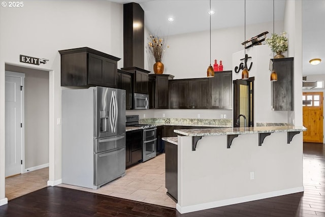 kitchen featuring light wood-style floors, a towering ceiling, light stone counters, and appliances with stainless steel finishes
