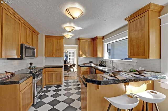 kitchen with light floors, a peninsula, a sink, stainless steel appliances, and a kitchen bar