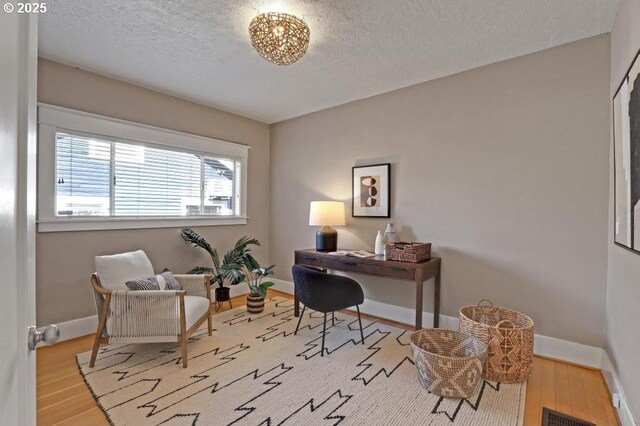 office area with visible vents, a textured ceiling, baseboards, and wood finished floors