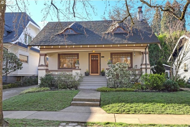 view of front of house featuring a chimney, covered porch, and a front yard