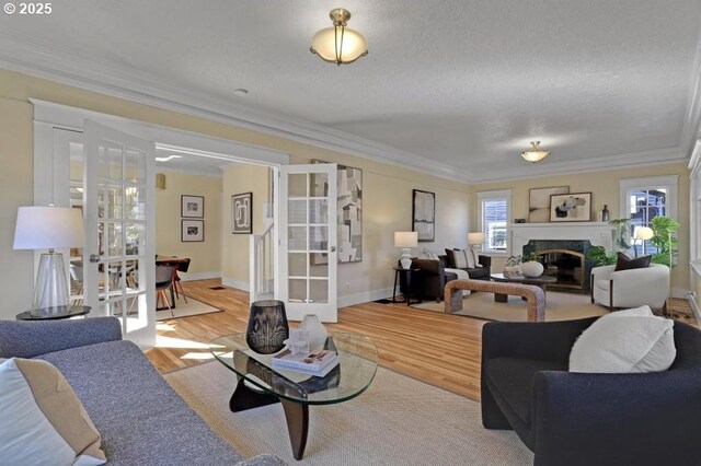 living room with wood finished floors, baseboards, ornamental molding, french doors, and a glass covered fireplace