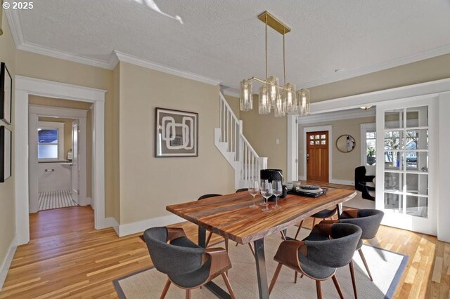 dining space with stairs, a textured ceiling, light wood-style flooring, and ornamental molding