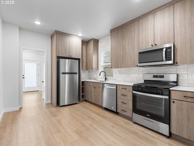 kitchen with light brown cabinetry, sink, light wood-type flooring, appliances with stainless steel finishes, and backsplash