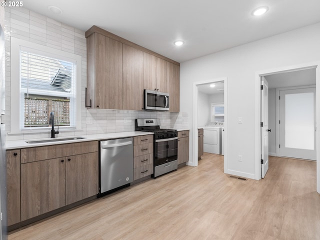 kitchen featuring sink, light hardwood / wood-style flooring, appliances with stainless steel finishes, separate washer and dryer, and decorative backsplash