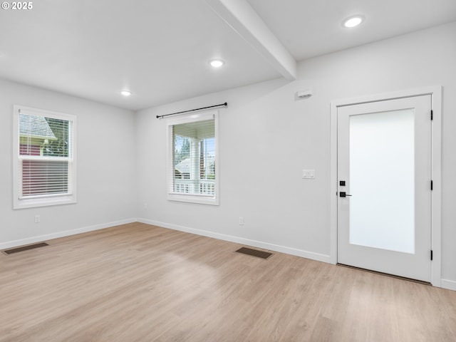 empty room featuring beamed ceiling, a healthy amount of sunlight, and light hardwood / wood-style flooring