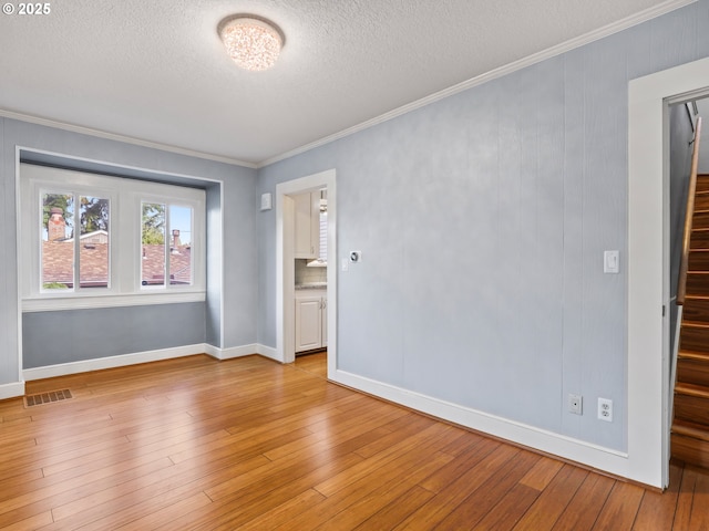 empty room featuring a textured ceiling, light hardwood / wood-style floors, and crown molding