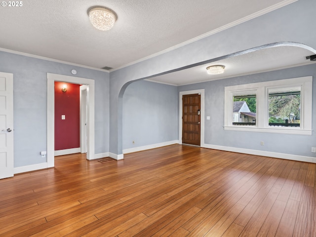 empty room with a textured ceiling, hardwood / wood-style floors, and crown molding