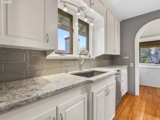 kitchen featuring dishwasher, light hardwood / wood-style floors, sink, white cabinets, and tasteful backsplash