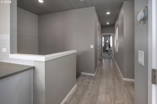 hallway with light wood-type flooring, recessed lighting, baseboards, and an upstairs landing