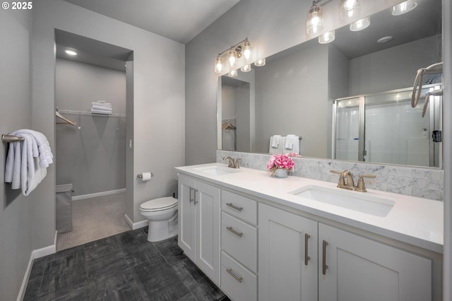 bathroom featuring a sink, a walk in closet, a stall shower, and toilet