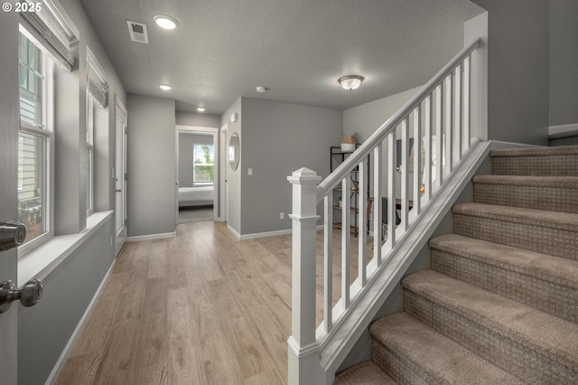 stairway with a textured ceiling, baseboards, wood finished floors, and visible vents