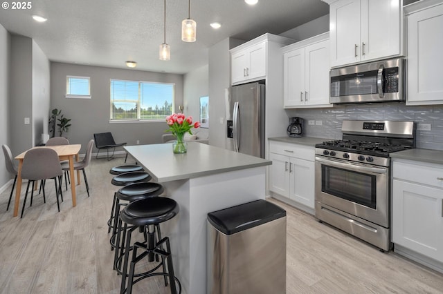 kitchen with a kitchen island, stainless steel appliances, light wood finished floors, and a kitchen bar