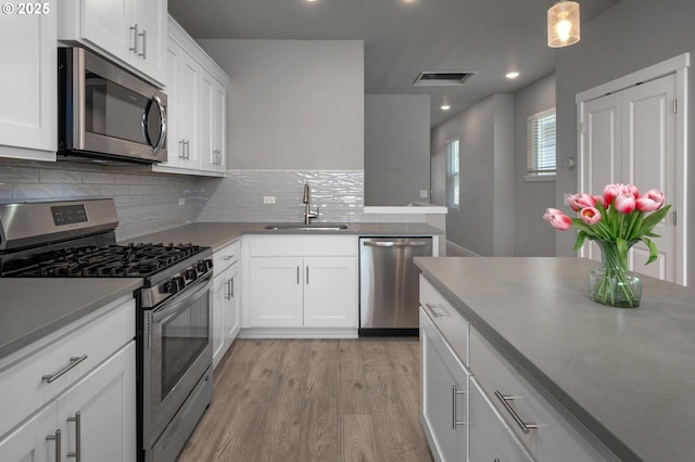 kitchen with a sink, light wood-style flooring, stainless steel appliances, tasteful backsplash, and visible vents