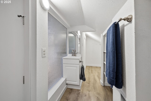 bathroom with wood-type flooring, vaulted ceiling, vanity, and a textured ceiling