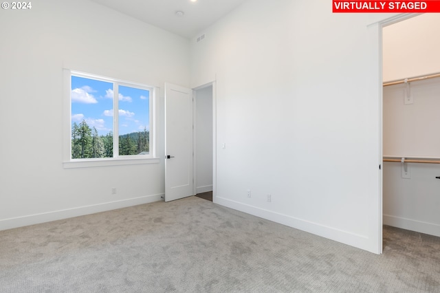 unfurnished bedroom with light carpet, baseboards, a walk in closet, and a closet