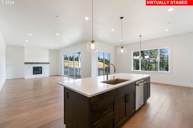 kitchen featuring decorative light fixtures, light countertops, a kitchen island with sink, a sink, and light wood-type flooring