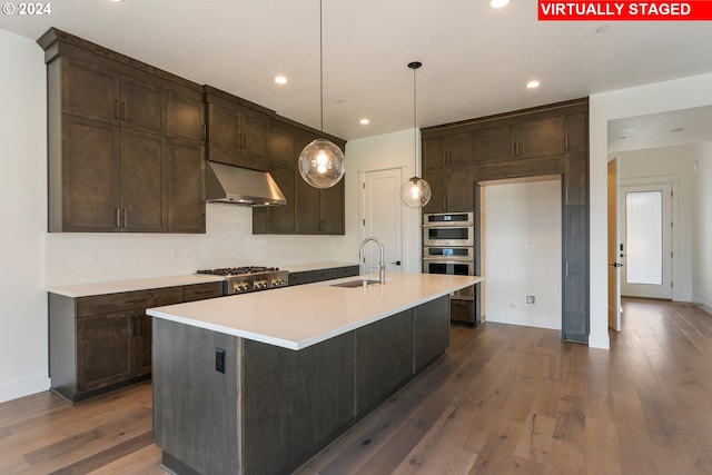 kitchen with pendant lighting, a center island with sink, light countertops, a sink, and wall chimney exhaust hood