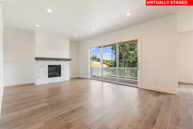 unfurnished living room with light wood-style flooring, a premium fireplace, baseboards, and recessed lighting