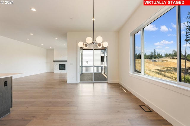 unfurnished dining area featuring a healthy amount of sunlight, recessed lighting, a glass covered fireplace, and light wood-style floors