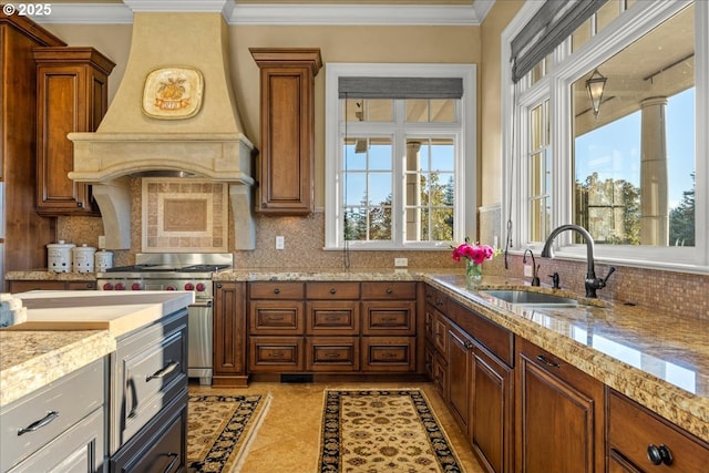 kitchen featuring tasteful backsplash, sink, high end stainless steel range oven, light stone countertops, and custom range hood